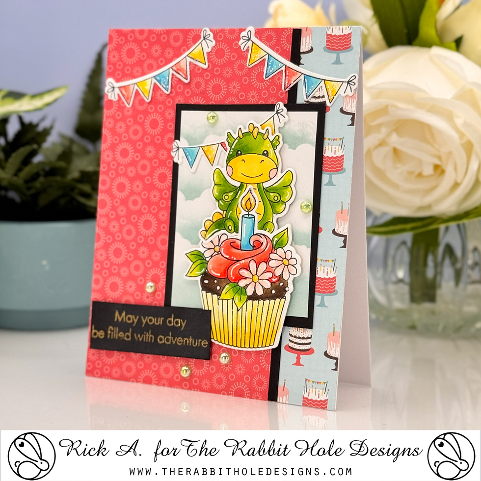 Cheerful card with a green dragon on a cupcake, surrounded by flowers. Background has colorful bunting and patterns. Text: "May your day be filled with adventure."