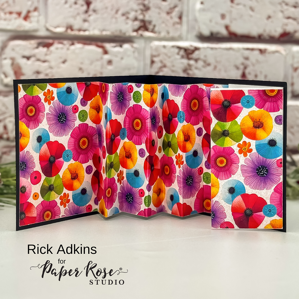 Colorful floral card with red, purple, and orange flowers on a table. Text reads "Rick Adkins for Paper Rose Studio." Brick-like background.