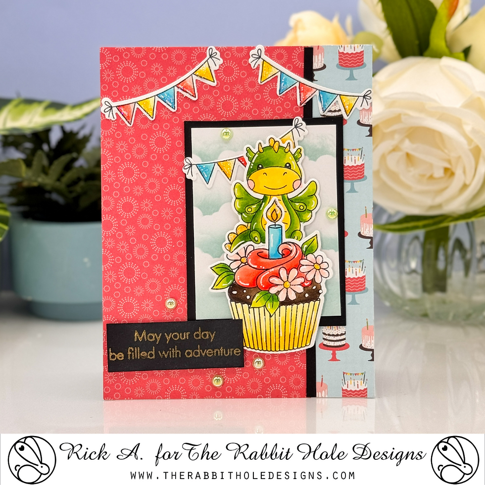 A card with a frog atop a cupcake with a lit candle, surrounded by colorful banners on a patterned red and blue background, text: "May your day be filled with adventure."
