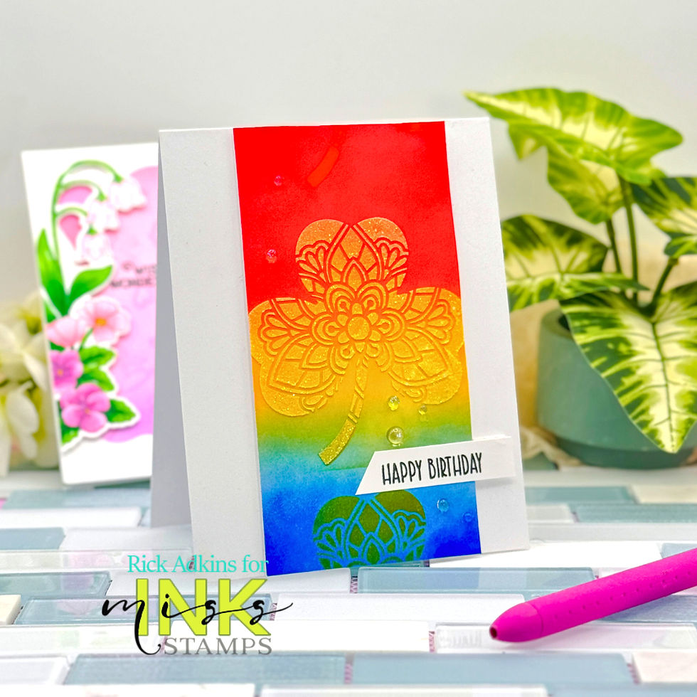 Rainbow card with floral design and "Happy Birthday" text. Background has a plant and another card with floral art in soft colors. Bright setting.