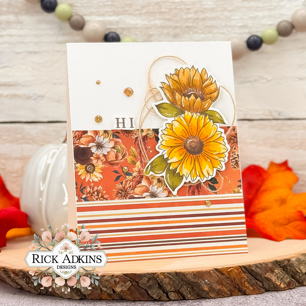 Greeting card with orange floral design, sunflowers, and "HI" text. Set against wood slice, with autumn leaves and beaded garland.
