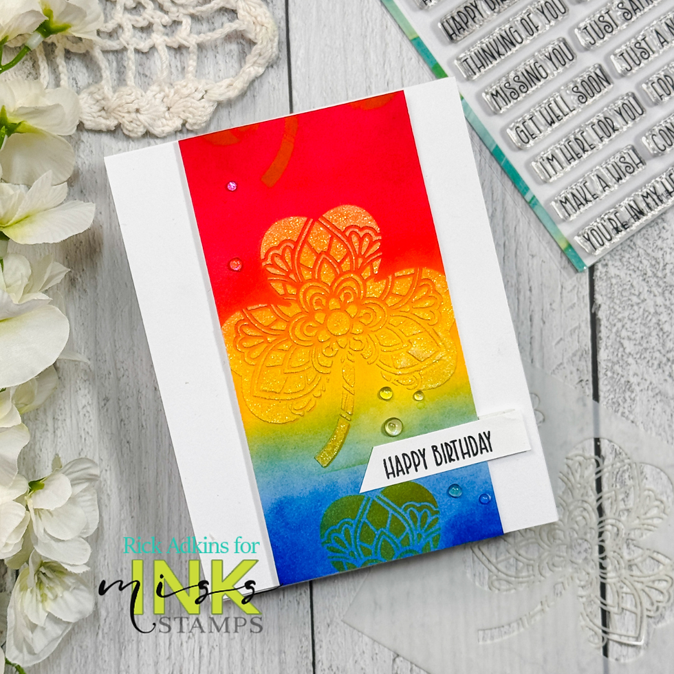 Colorful card with a floral mandala on a red to blue gradient. Text “Happy Birthday” at the bottom. White flowers and stamps in the background.