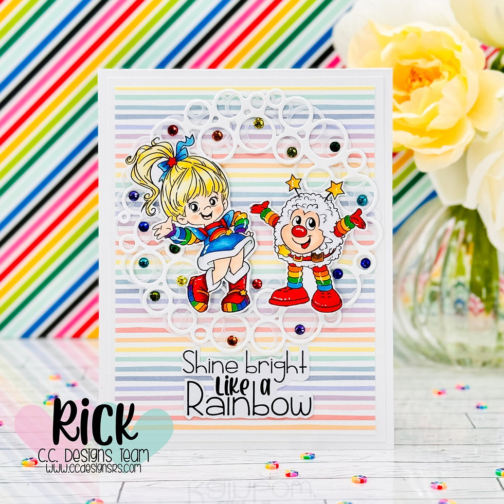 Colorful card with cartoon girl and clown dancing, surrounded by gems on rainbow stripes. Text reads "Shine bright like a rainbow."