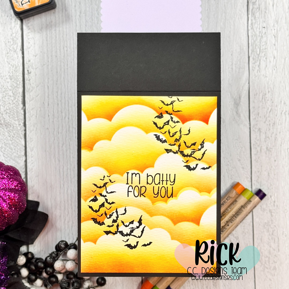 A card with bats flying over yellow-orange clouds reads "I'm batty for you." Pencils and glittery decor surround it on a wooden surface.