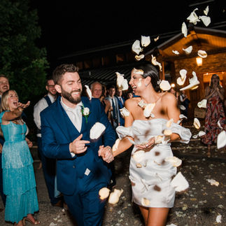 newlywed couple leaving their reception, showered with flower petals by guests