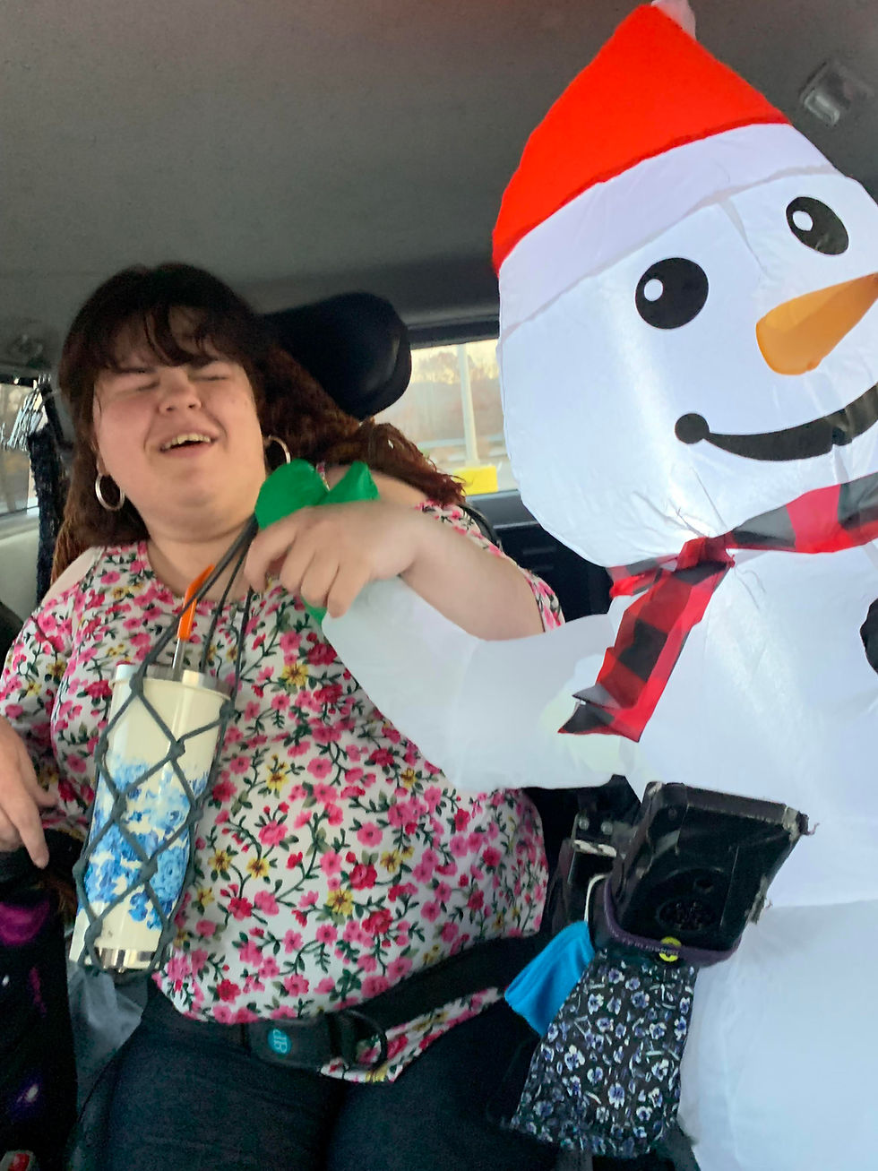 Me in a floral shirt , all smiles in a car beside a large inflatable snowman, my car buddy, with a red hat, creating a festive, cheerful scene