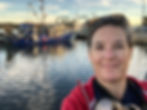 woman at marina holding camera with fishing boats in the background