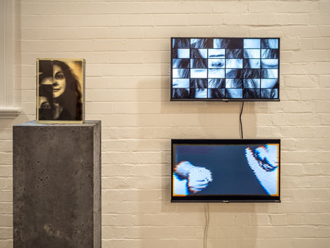 Gallery wall with a portrait on a concrete pedestal and two wall-mounted screens showing fragmented black-and-white face images