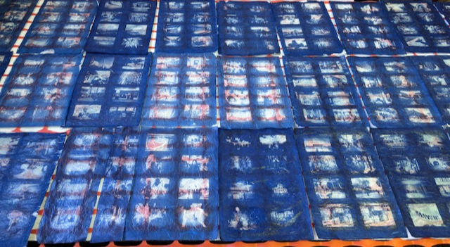 Rows of blue fabric panels with faded printed images are spread on the ground, creating a repetitive patterned display.