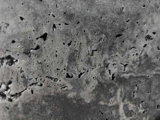 Black-and-white close-up of cracked, pitted concrete or stone with rough texture and scattered dark holes.