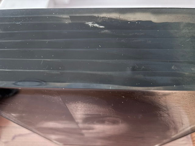 Close-up of a black slatted cover over a sepia-toned photo, showing part of a person’s face beneath it.