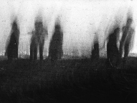 Blurred silhouettes of five figures stand on a dark field with a foggy, white background, creating a mysterious and eerie mood.