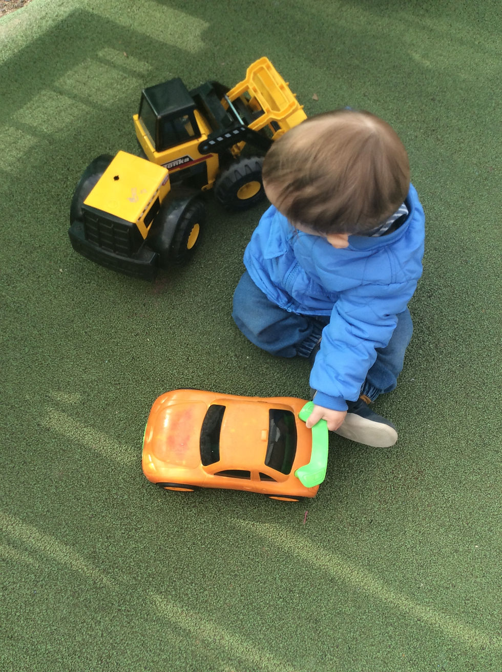 A child sitting on grass and engaging in imaginative play with toy cars