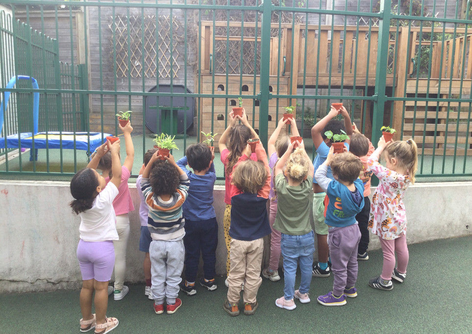 Kidz Kabin Nursery Pembroke Studios Muswell Hill - group of children with their backs facing the camera holding up their plant pots