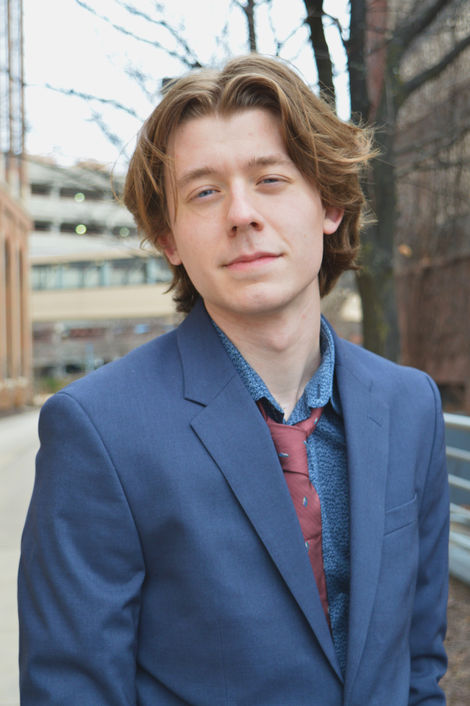 Portrait of man in professional attire with city background blurred, DSLR image.