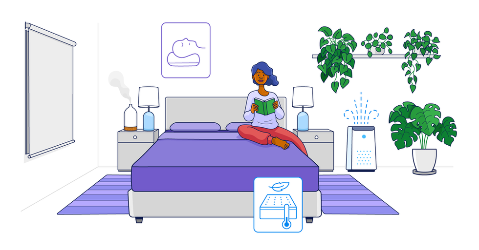 A woman with curly hair is sitting cross-legged on a bed, reading a green book in a modern, well-decorated bedroom with plants, a humidifier, and minimalist decor.