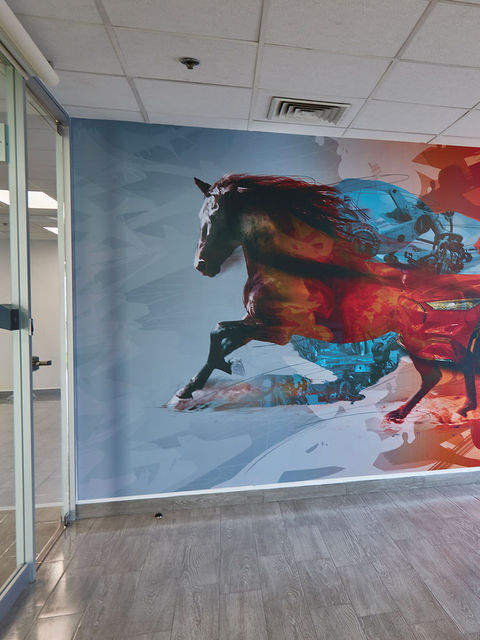 Mural colocado en la pared de una sala audiovisual. Es una composición gráfica de un caballo galopando hacia la izquierda, seguido por un Mustang Mach-E rojo.