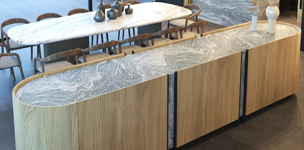 Mueble trinchador para comedor en una terraza. El mueble está hecho de madera combinada con mármol en tonos grises y blancos. El mueble tiene forma elíptica. Detrás de este mueble se aprecia una mesa grande, también de mármol, con 12 sillas de madera.