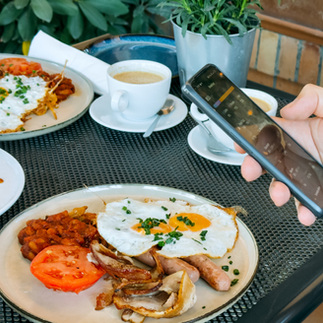 restaurant table with plates of food and cups of coffee and a hand holding a smart phone logging food intake