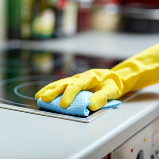 hand wearing a yellow rubber cleaning glove with a blue rag, wiping the surface of a stovetop