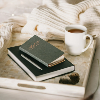 breakfast tray on bed with stack of journals and cup of coffee, next to a with throw blanket