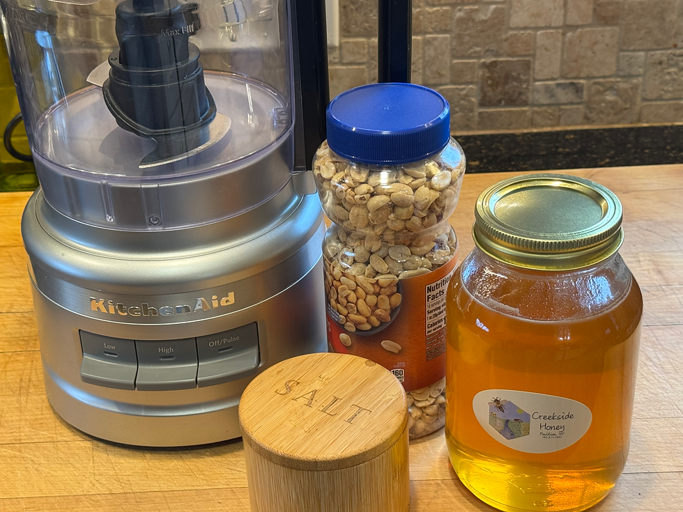 food processor, peanuts, honey and salt on a large wooden cutting board
