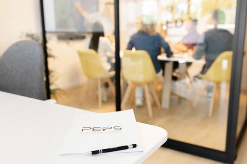 Bloc-notes et stylos PEPS sur une table de réunion vitrée, ambiance professionnelle – par Julien Stevens Photography