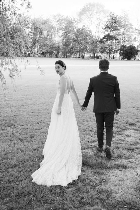 La mariée regarde en arrière pendant qu’elle marche main dans la main avec son mari, photo en noir et blanc – par Julien Stevens Photography