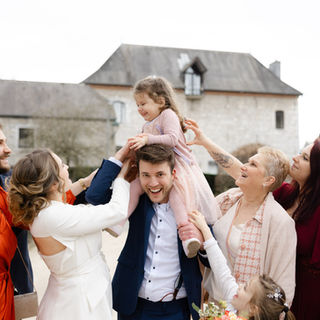 petite demoiselle d'honneur sur les épaules du marié entourée de ses proches qui rient ensemble par Julien Stevens Photography