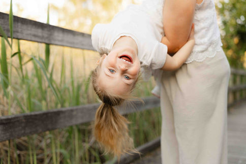 A little girl laughing upside down, clinging to an adult's arms – by Julien Stevens Photography