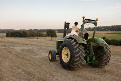 Mariés au volant d’un vieux tracteur vert, roulant dans un champ doré à la lumière du soir – par Julien Stevens Photography