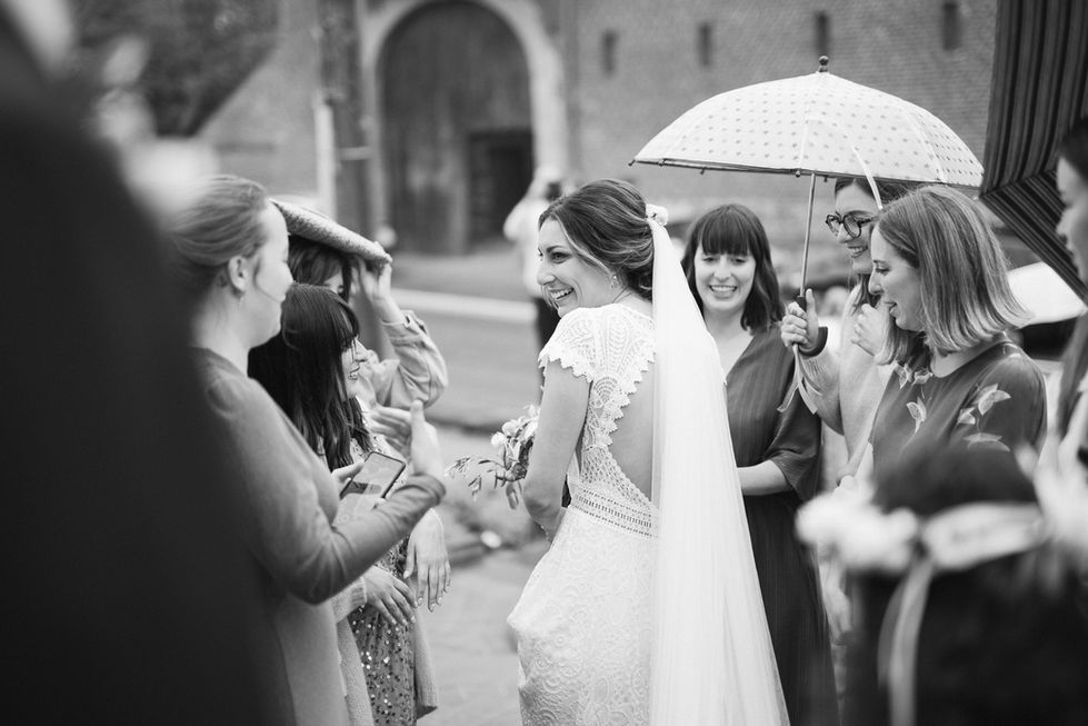 Mariée souriante entourée de ses proches sous un parapluie, photo en noir et blanc – par Julien Stevens Photography