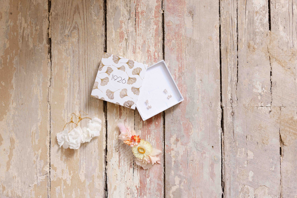 Vue d’en haut sur les accessoires de mariage de la mariée : bracelet, boîte et bijoux sur un sol en bois – par Julien Stevens Photography