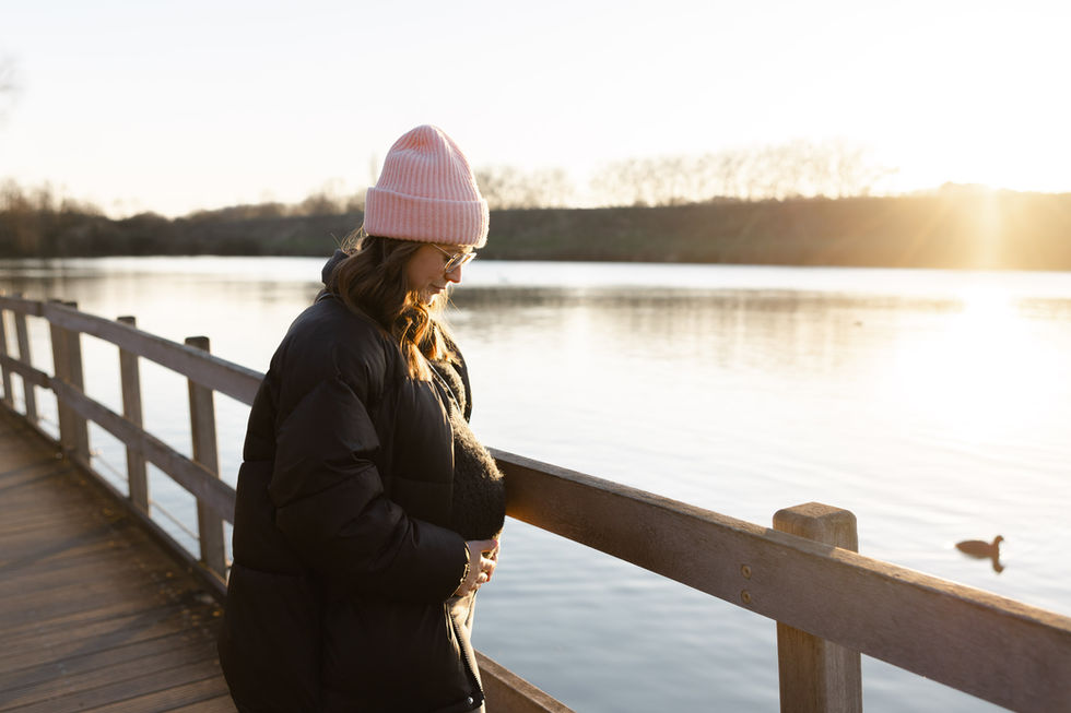 A pregnant woman standing on a wooden pontoon, contemplating the lake at sunset – by Julien Stevens Photography