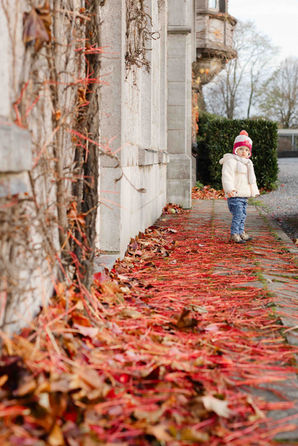 Petite fille marchant dans une allée couverte de feuilles rouges, ambiance automnale – par Julien Stevens Photography