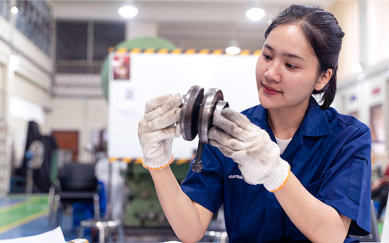 Worker inspecting mechanical part in workshop.