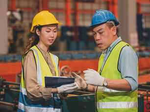 Two manufacturing workers discussing precision production in Thailand.