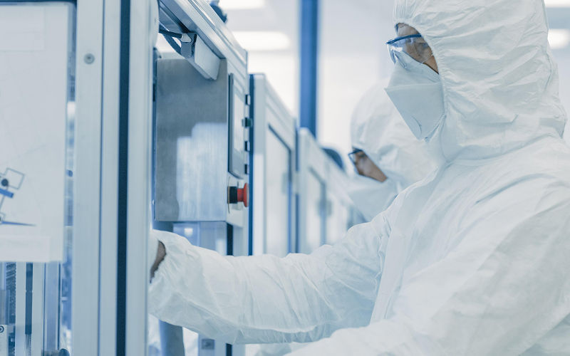 Technician in a cleanroom operating precision manufacturing equipment.