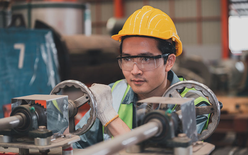 Technician in safety gear manually adjusting industrial machinery controls.