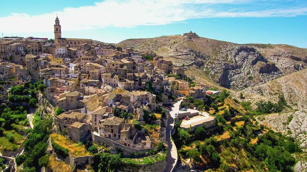 Sziklás hegyoldalra épült kőfalú mediterrán falu, Bocairent , templomtoronnyal, kék ég alatt, napsütötte, nyugodt látkép.