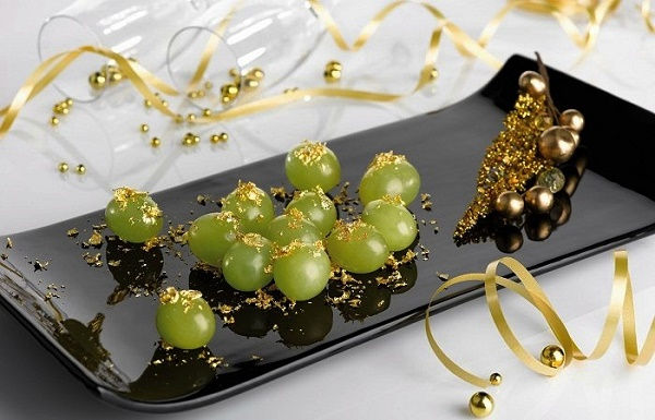 Zöld szőlő arany díszítéssel fekete tálon, körülötte arany szalagok. Elegáns, ünnepi hangulat egy fényes háttérrel. Spanyol szilveszter szokások 12 szőlőszem fogyasztása.