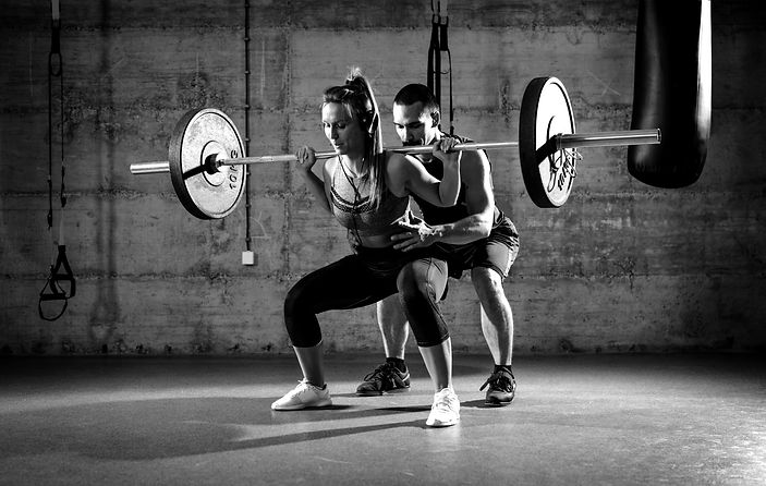 Young woman doing squat exercise at the gym with a personal trainer._edited.jpg