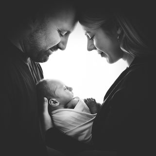 Black-and-white portrait of two adults gently holding a sleeping newborn