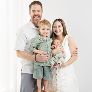 Family of four smiling with an older child seated and a newborn held