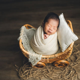 Newborn wrapped in a cream blanket sleeping inside a wicker baby carriage