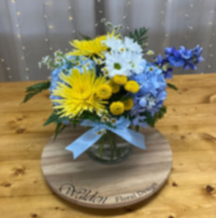 Decorative arrangement titled 'Baby Blue' showcasing a delightful combination of delphinium, mums and daisies.