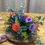 Thumbnail: A video of a flower arrangement containing orange roses, pink spray roses, purple lisianthus, blue delphinium, and solidago