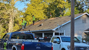 Roofers working on a roof, trucks parked, trees, cloudy sky, Pinula Roofing.