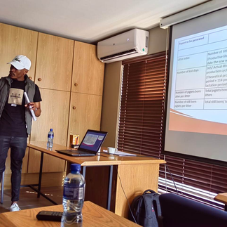 Johannes delivering his final presentation at CS Vet's main office. Laptop on a desk next to him and presentation up on a screen behind him.