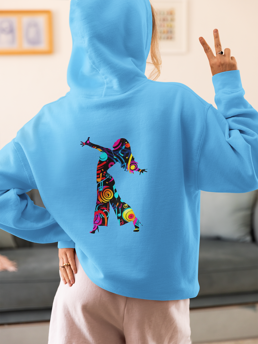 Woman facing away with 1 hand in the air wearing a blue hoodie with hood up & female dancer design with colours